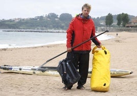 El sueco Jonas Böhlmark, con su mochila amarilla y su tabla de pádel surf detrás, en la playa de Luanco.